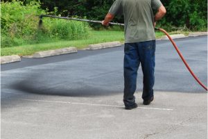 Asphalt Sealcoating by a worker with a sprayer